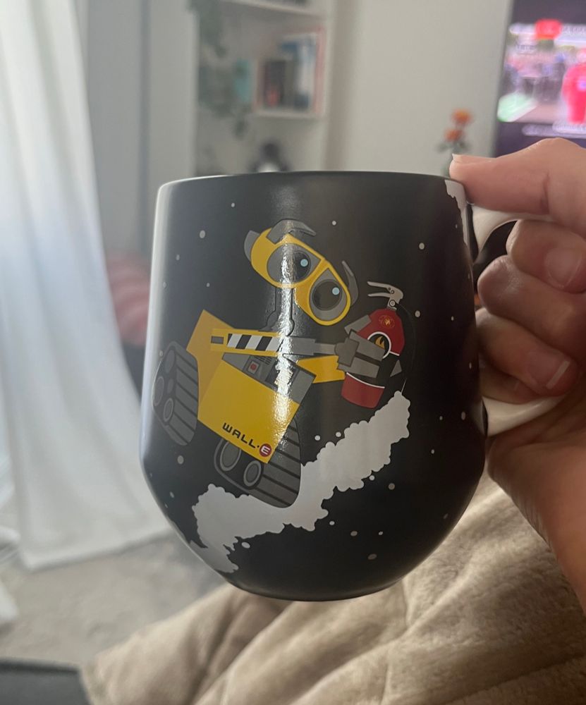 Black mug with Wall-e on the front holding a fire extinguisher floating through space 