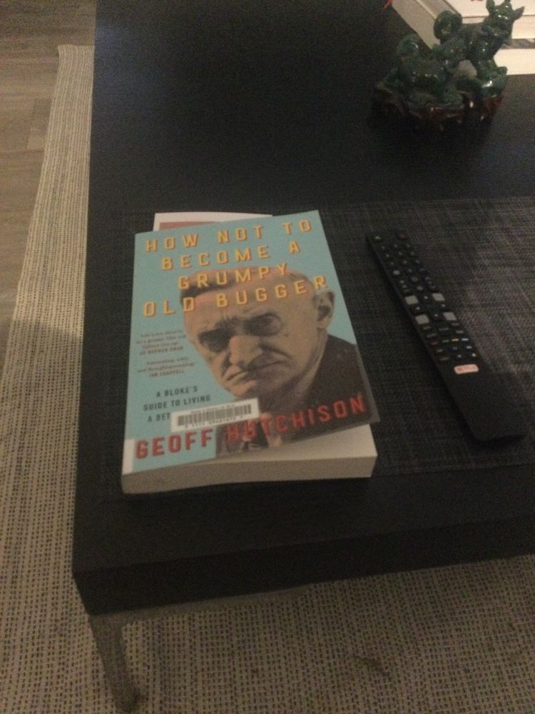 Photograph of a book entitled How not to be a grumpy old bugger sitting on a coffee table besides a remote control