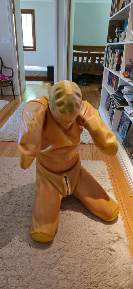 A boy trapped in a latex bitchsuit. He sits on his knees and stares down at his crotch.