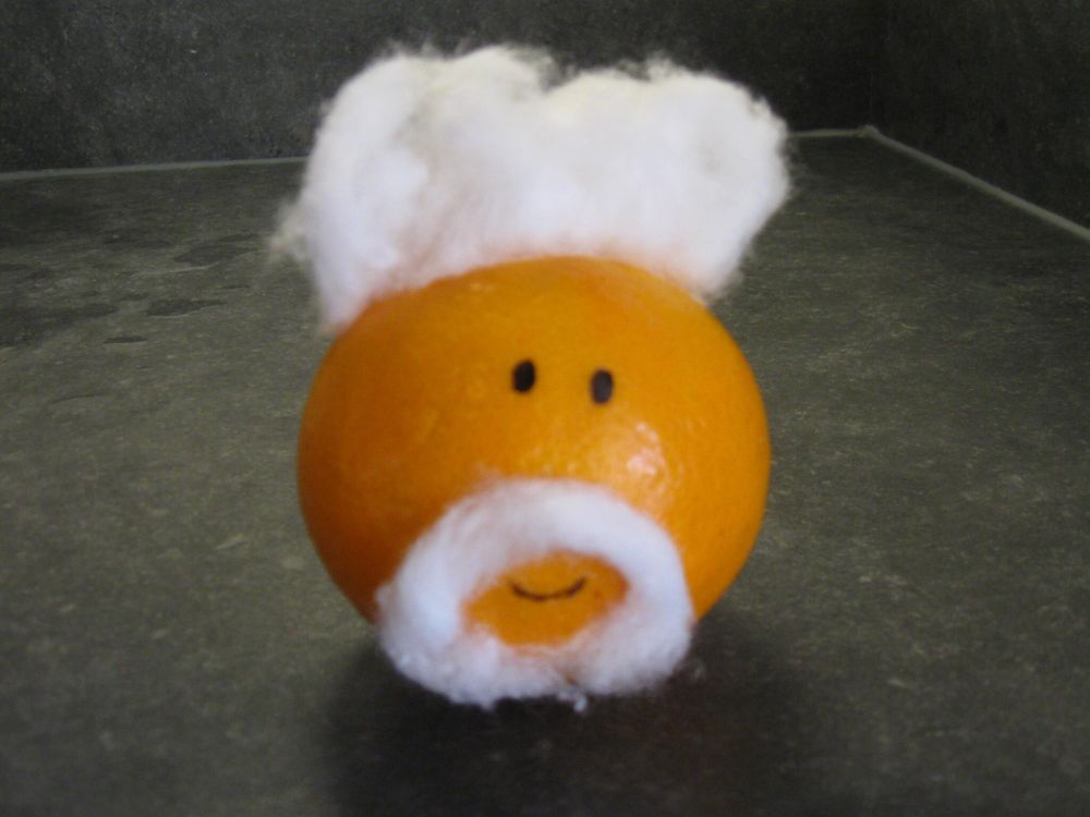 An orange with cotton wool stuck to it and a face drawn on in pen to make it look like Tom Jones.