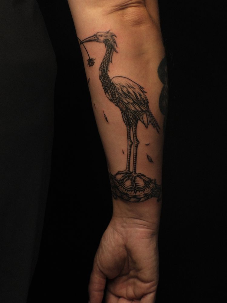 Woman’s arm (mine) showing from elbow to palm with a black fine line tattoo in a Vietnamese engraving style of a crane riding on the back of a wise old turtle 