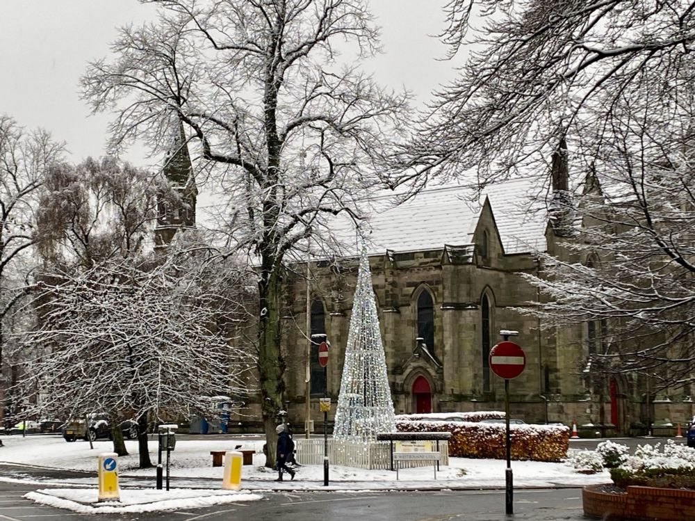 A church covered in snow with a Christmas tree outside 