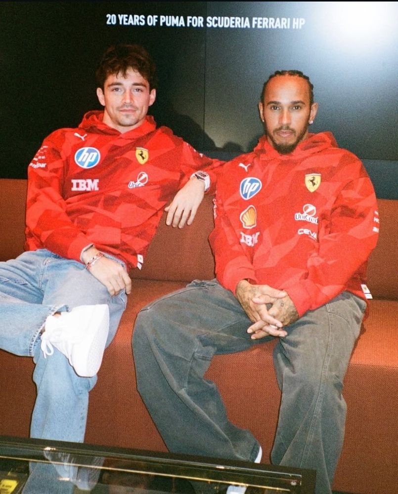 Charles Leclerc and Lewis Hamilton sitting together on a couch in their Las Vegas merch.