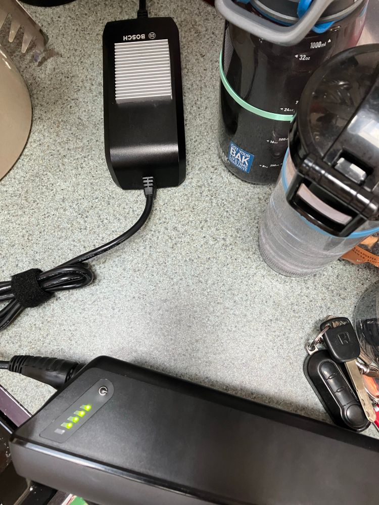 a Bosch eBike battery charger is shown with a new aluminum heat sink installed by the owner. the case was removed to cut away the plastic and allow the new heatsink to contact the internal heatsink. prior to this modification, all the heat produced by the switching power supply inside the charger was trapped by the case. high temperatures reduce the life of components.