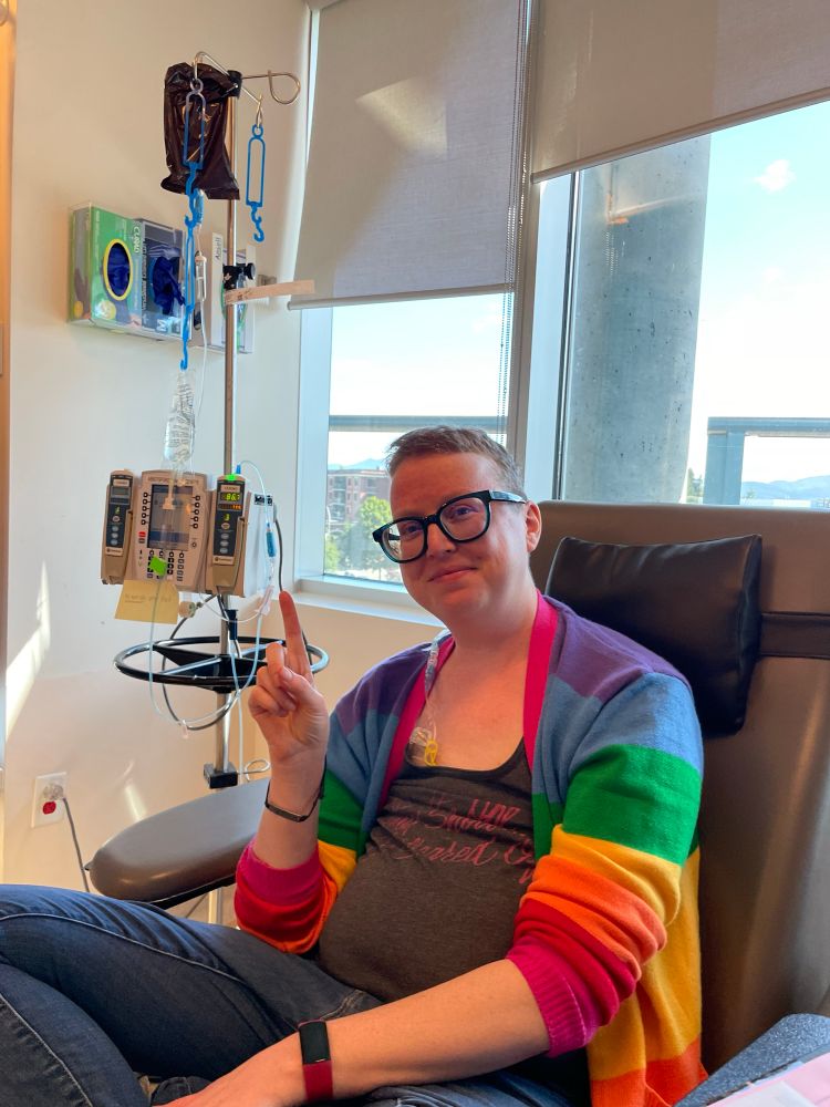 Andrea sits plugged into the chemo chair, holding up a number one. 