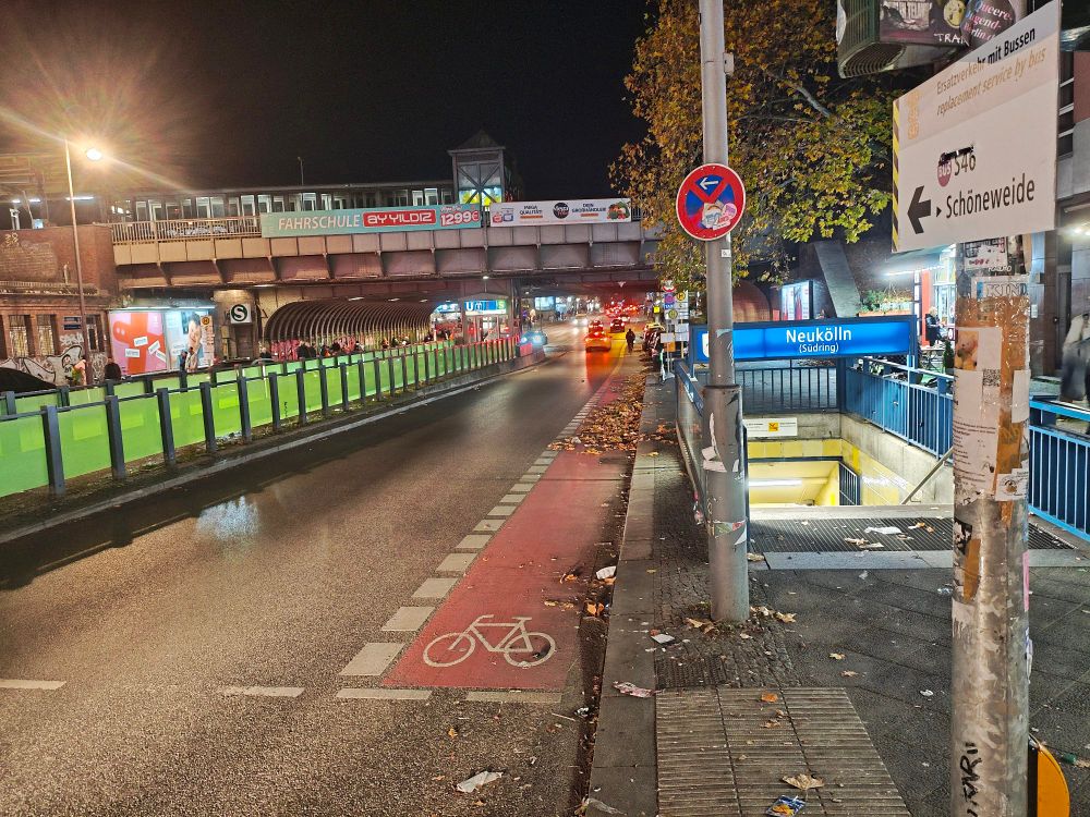 rechts der ubahn Eingang, neuKölln, dann eine Straße mit Radweg und eine Brücke über die Straße. Es ist Nacht.