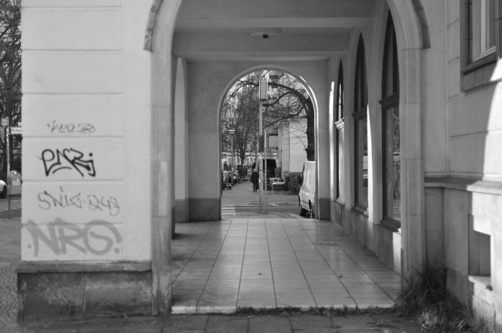 s/w. bogengang unscharf, der durchblick scharf auf laterne und parkende autos.