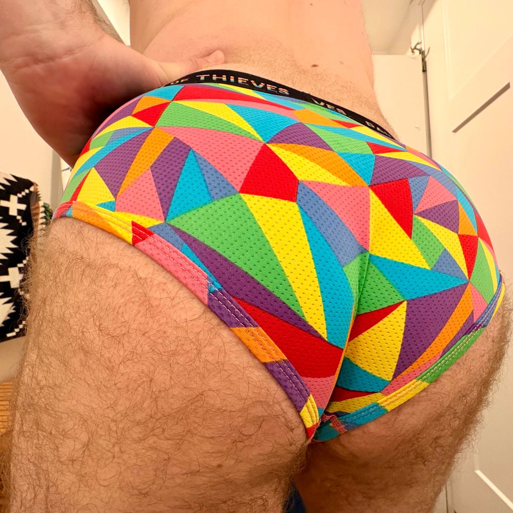 Brady posing in a pair of rainbow, geometrically patterned briefs, butt cheeks and fuzz spilling out the edges