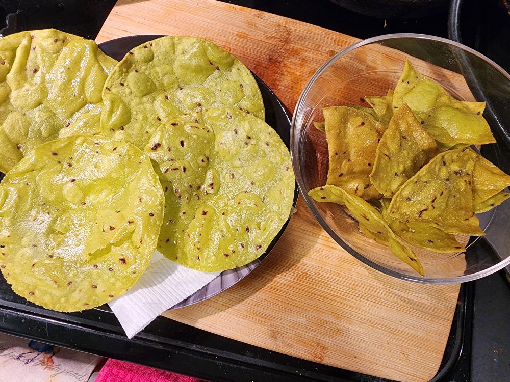 A cutting board on top of which sits a plate of four crunchy tostadas and a bowl of freshly made tortilla chips