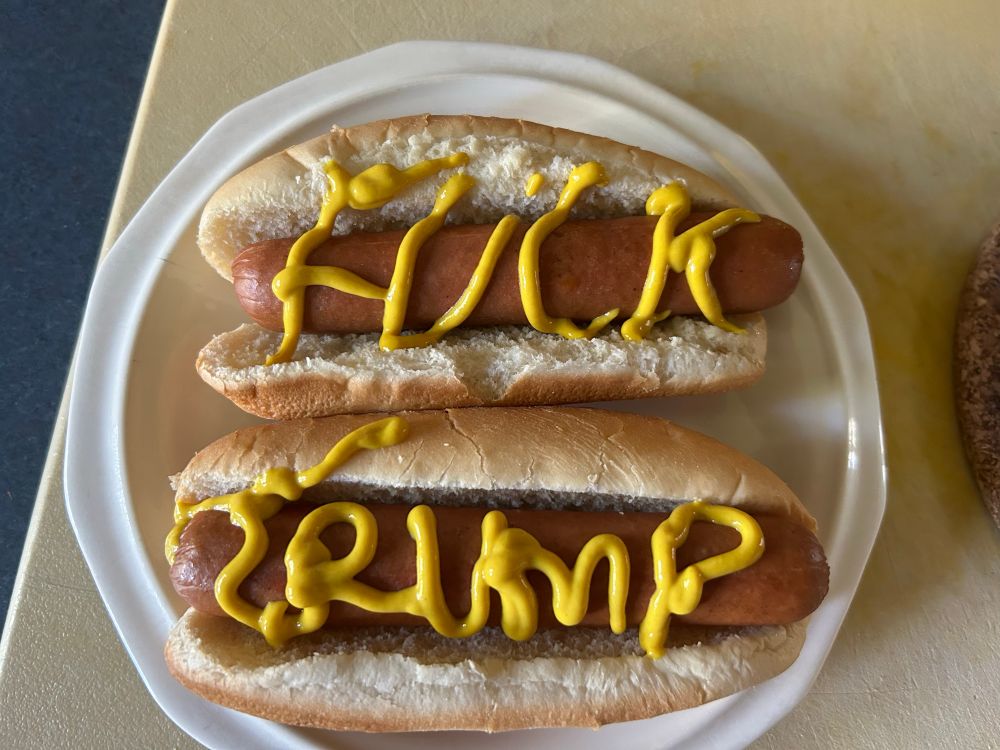 Two hot dogs with Fuck trump written with yellow mustard 