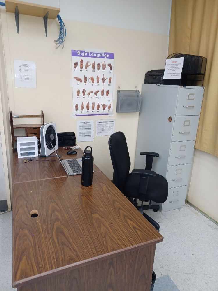 That same corner of the classroom with the desk, file cabinet, and chair. This time the desk is completely empty other than a laptop, water bottle, and some empty shelving units. All the trinkets, folders, and supplies are away in the file cabinet. It looks empty and lonely, as the school year is now over. 