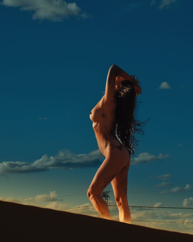 A woman stands o a sand dune ridge at sunrise, basking in the sun’s warmth..