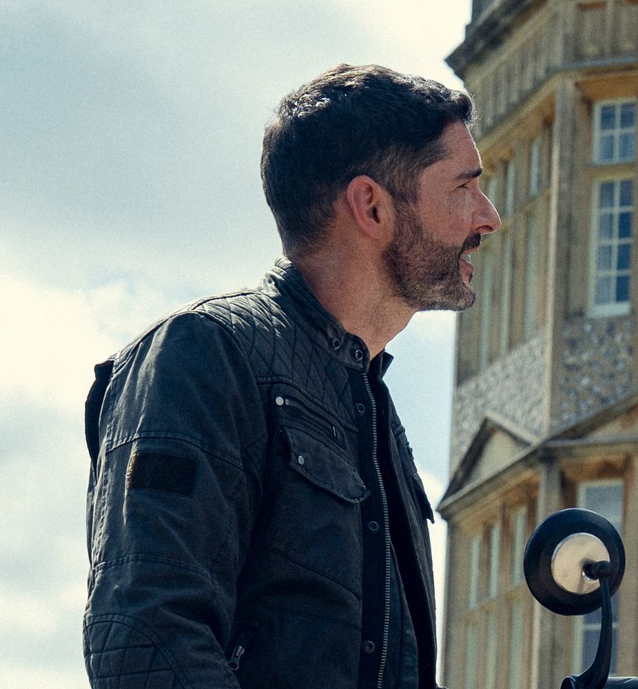 Side shot of Tom Ellis on a motorcycle in The Thursday Murder Club