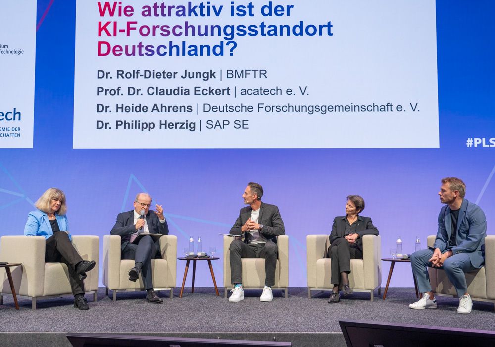Zwei Frauen und drei Männer sitzen in einer Panel-Runde auf einer Bühne und diskutieren
