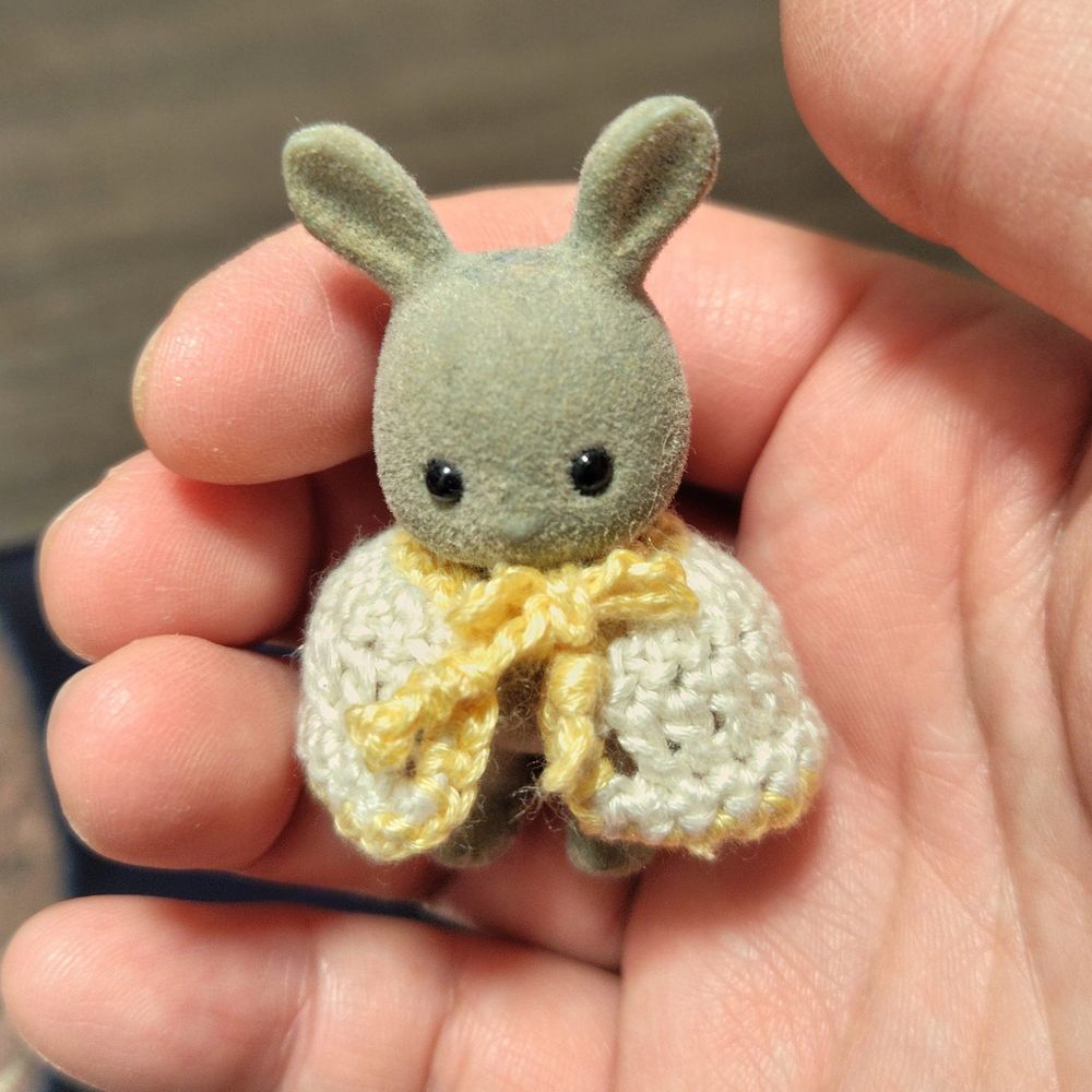 シルバニアファミリーのうさぎの赤ちゃんが、かぎ針編みのケープを着ている。