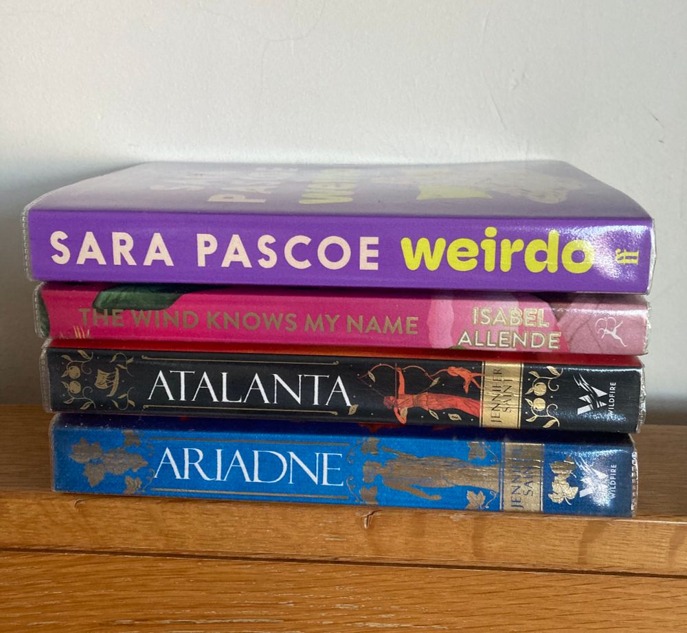 Neat pile of four paperback books: ‘Ariadne’ and ‘Atalanta’, both by Jennifer Saint; ‘The Wind Knows My Name’ by Isabel Allende, and ‘Weirdo’ by Sara Pascoe