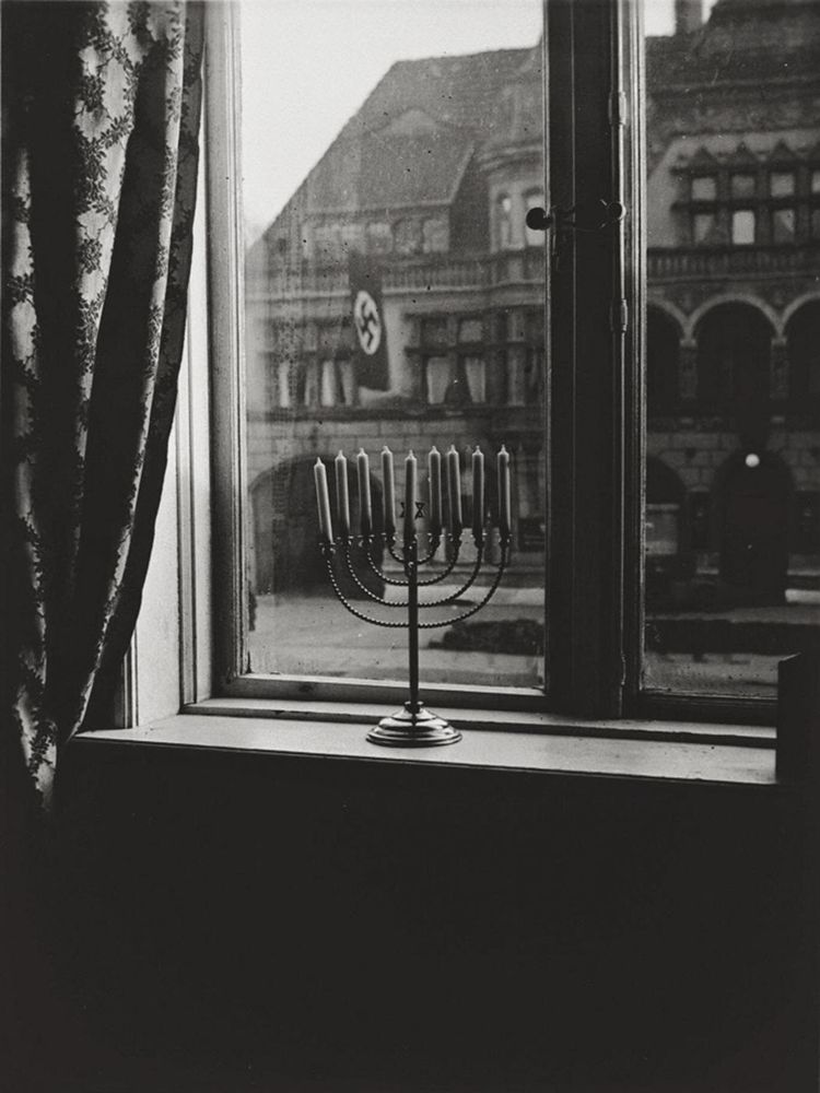 A menorah in a window facing an official looking building flying the swastika flag of Nazi Germany
