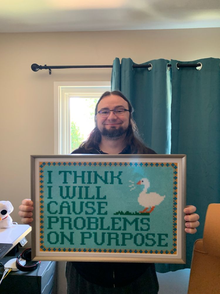 Me holding a big framed piece of art depicting the goose from untitled goose game honking with a caption of "I think I will cause problems on purpose"
