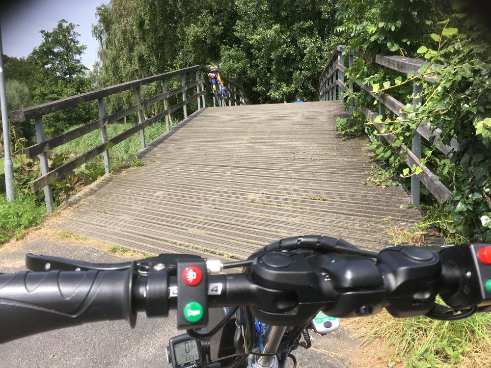 Een stuur van een elektrische aankoppelfiets, met daarachter een (te) steile brug. 