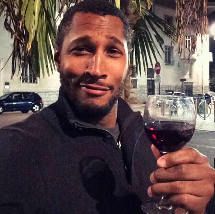 Boris Diaw, retired NBA player from France, holds up glass of wine, while smirking.