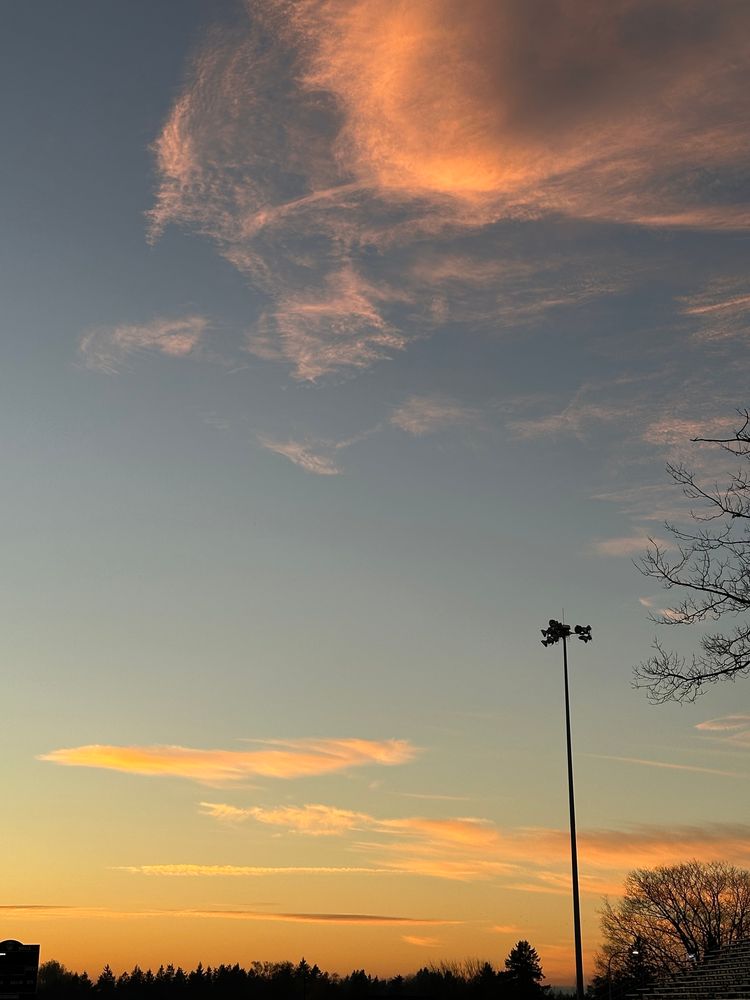 sunset from a high school track with a clear horizon vista, football scoreboard, unlit stadium light and trees along the edges, wispy pink clouds in the sky