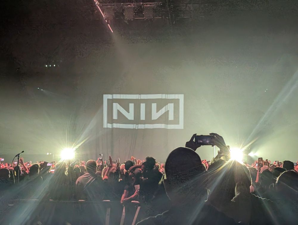a photo of the stage backdrop at the Nine Inch Nails show, featuring their NIN logo, with the sea of concert-goers in the pit taking photos and looking on, probably also enjoying being depressed for entertainment, in a seductive way