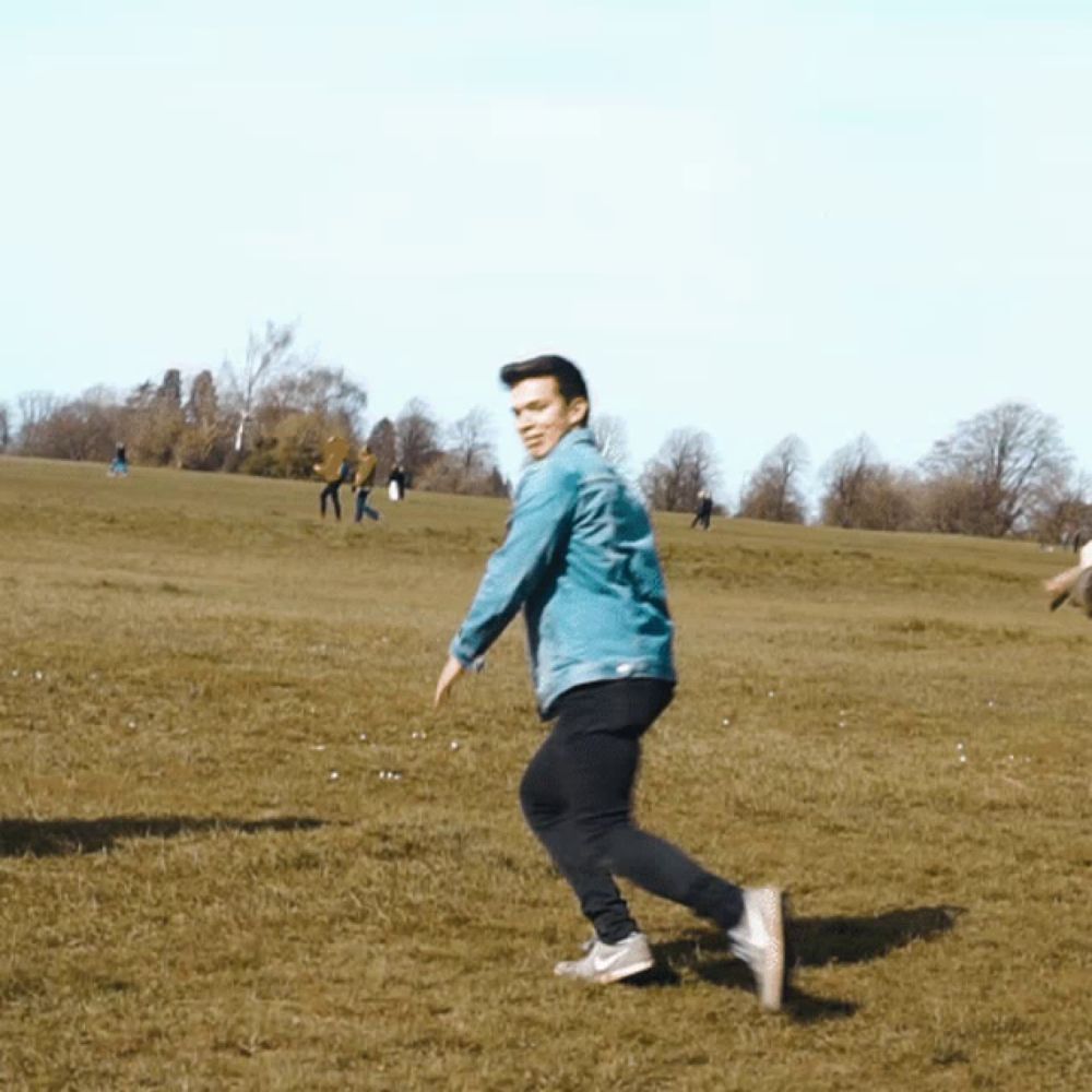 a man in a denim jacket is running on a grassy field