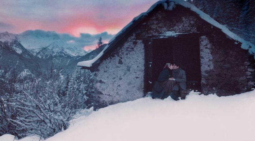 A screengrab from the 2024 Italian film Vermiglio, showing a young couple kissing at the entrance to a stone hut in the snowy Italian Alps.