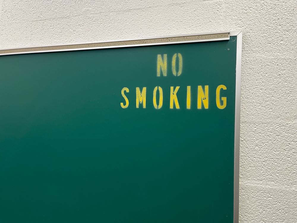 A picture of a blackboard with the message “no smoking” spray painted in the top corner
