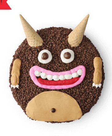 photograph of a round cake covered in chocolate crunchies with ice cream cone horns, eyes, a wide pink smile, little arms and a belly indicating a friendly little monster guy