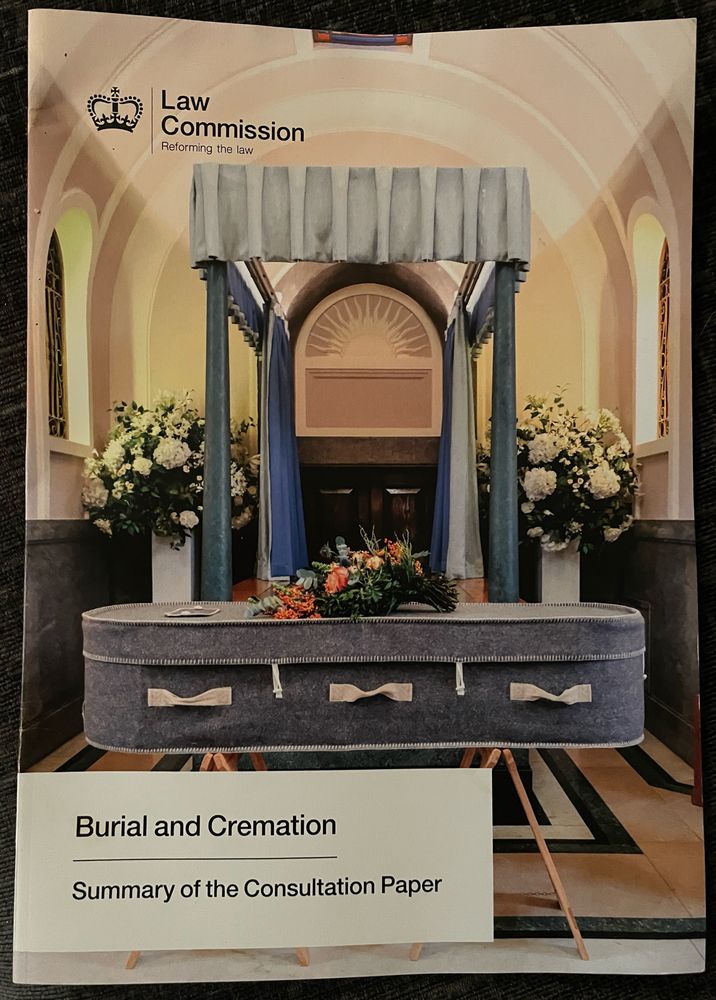 Photo shows the front cover of a booklet featuring a great woollen coffin on trestles in a crematorium. The booklet is entitled ‘Burial and Cremation, Summary of the Consultation Paper’ and is produced by The Law Commission.