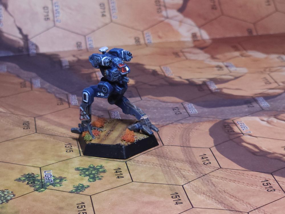 A Flea light battlemech painted blue with white accents. The paint scheme belongs to the Marian Hegemony VI Legio. The Flea has had its arm mounted lasers replaced with a pair of machine gun arrays and a rocket launcher pod has been added to the right torso. The mech is stepping over a road, past a crossing sign
