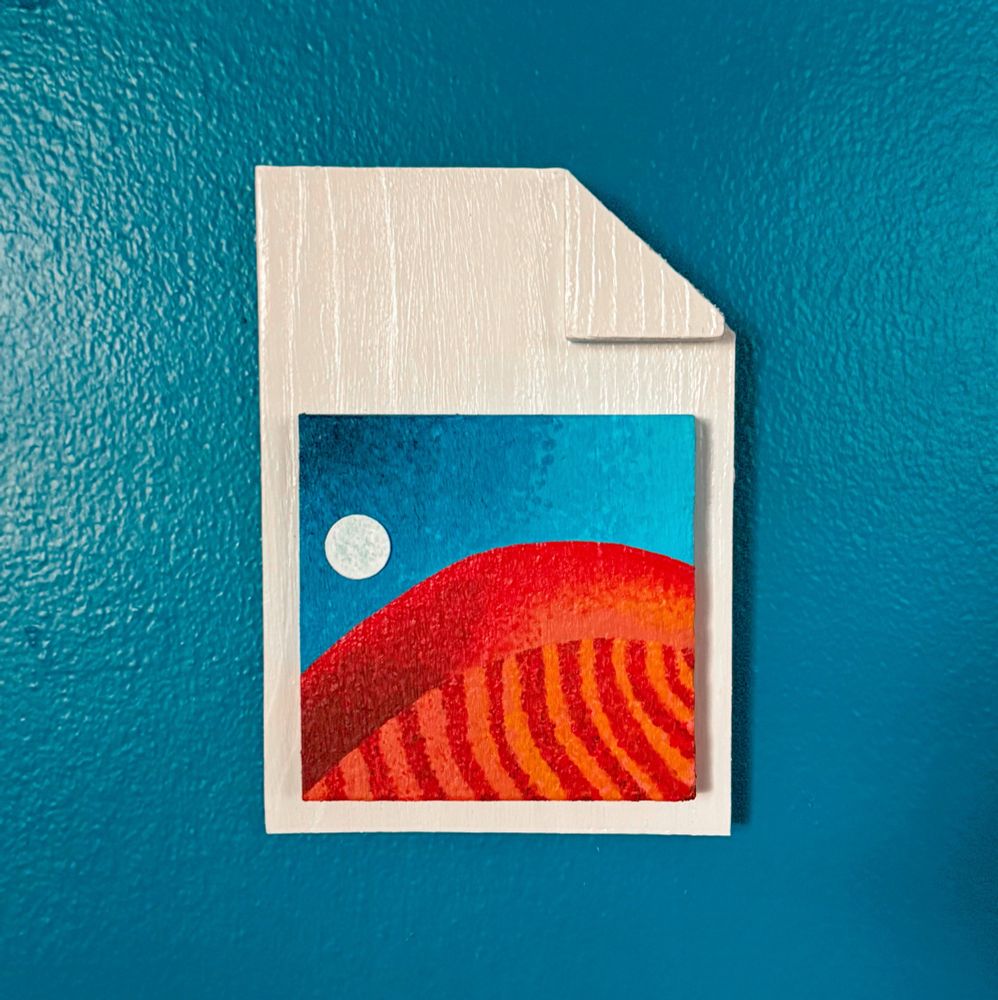 A physical version of a jpg icon hanging on a blue wall. The icon is a piece of paper with the top right corner “folded over”. There is a “photograph” painting of the Windows XP wallpaper, Red Moon Desert, which features a red planet and a lone moon in the corner.
