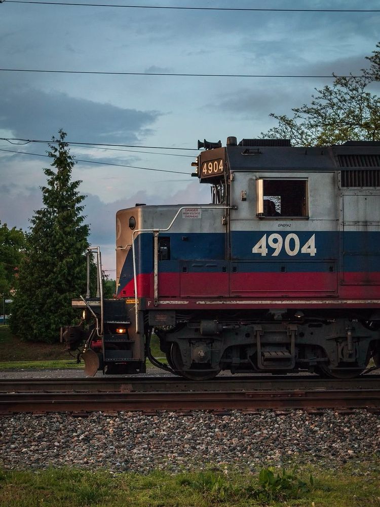 A side view of a Metro-North train running along the tracks on a cloudy evening. 