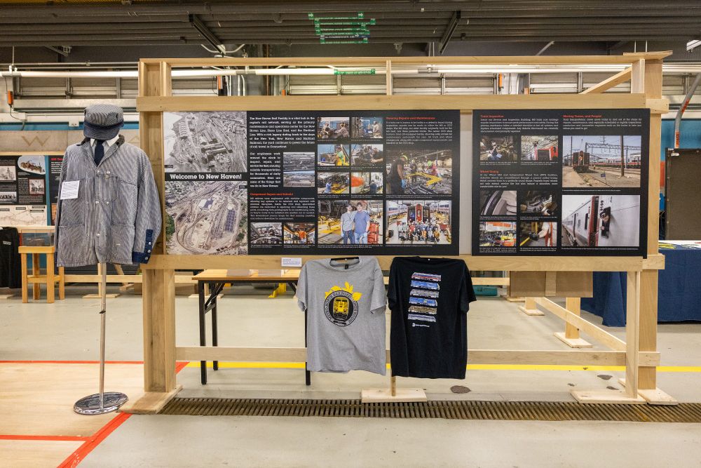 An exhibit inside the New Haven Yard, featuring two T-shirts and a conductor outfit, as well as two hanging posters detailing the yard. 