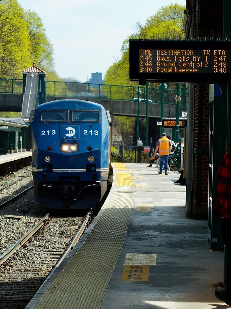 A Metro-North train pulling into Poughkeepsie station during the daytime, with people waiting on the platform.