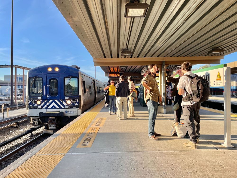 A Metro-North train pulling into Croton-Harmon station during golden hour, with people waiting on the platform.