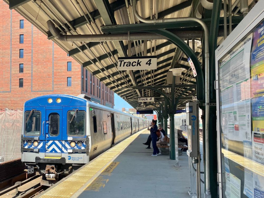 A Metro-North train pulling into Harlem-125th Street station on a sunny day, with people waiting on the platform.