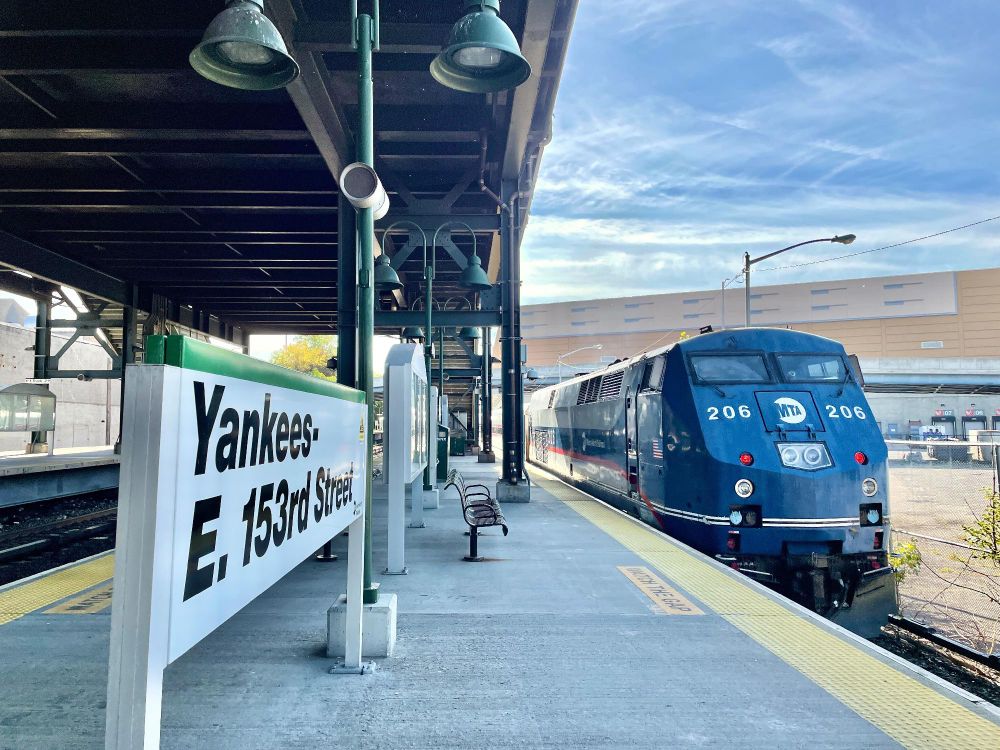A Metro-North diesel train pulling away from Yankees-E. 153rd Street station on a sunny day.