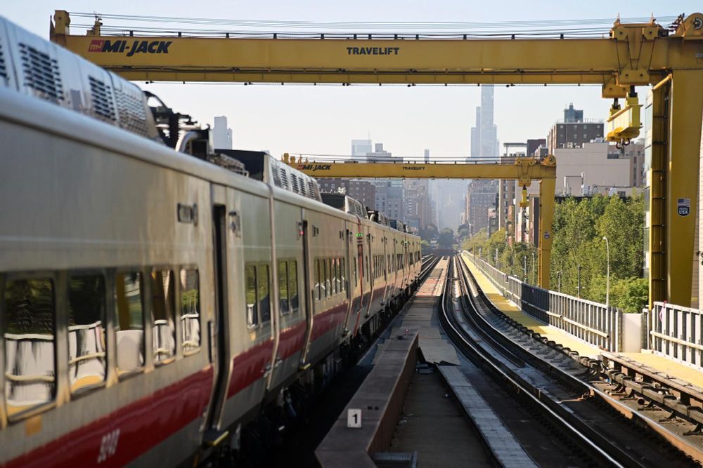 A Metro-North train running along the tracks, underneath the viaduct, on a sunny day.