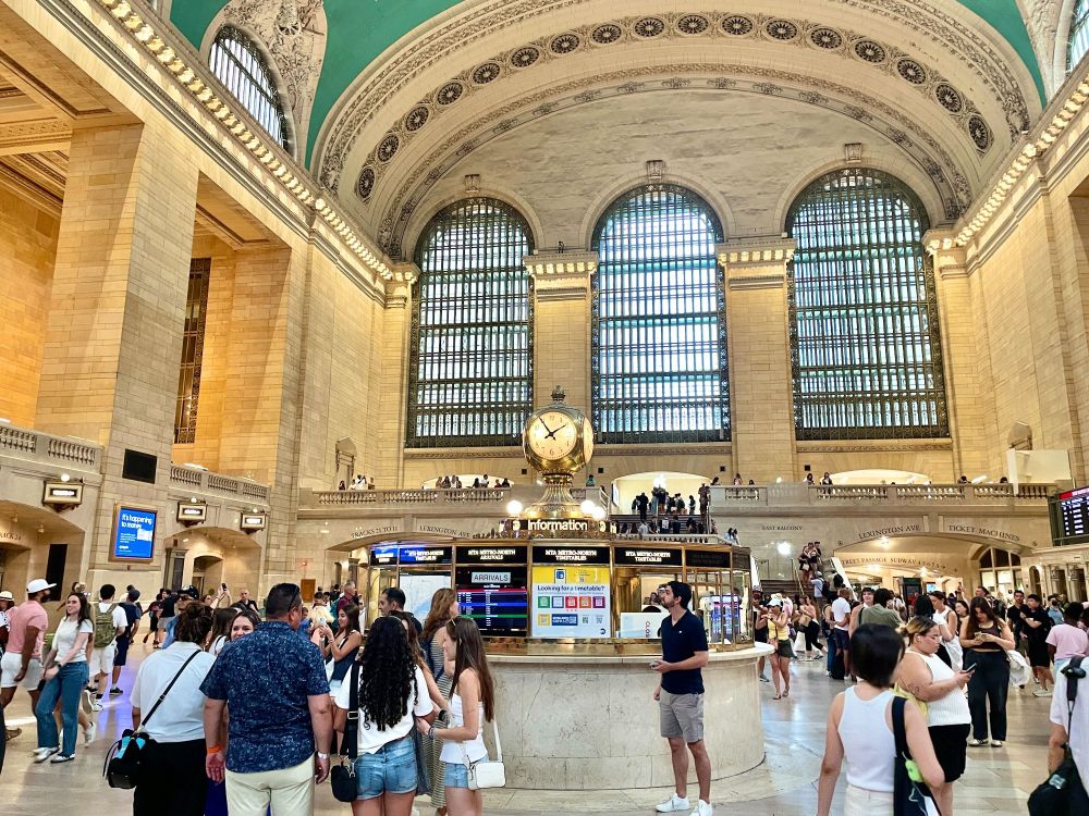 The interior of Grand Central Terminal station, by the clocktower, with many people walking through.