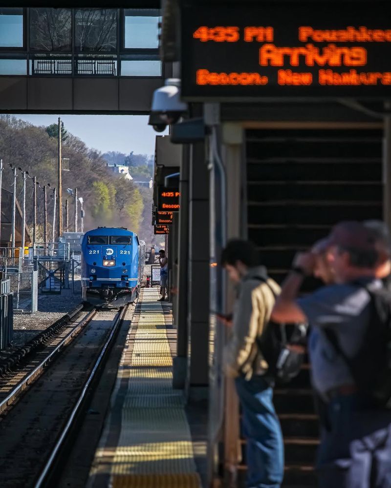 A Metro-North train pulling into Croton-Harmon station during the daytime as people wait on the platform.