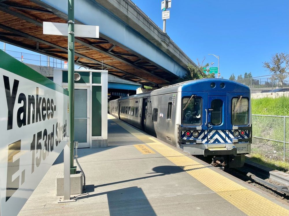 A Metro-North train pulling into Yankees-E. 153rd Street station on a sunny day.