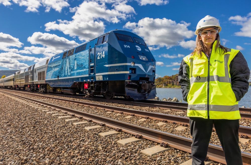 Emily Moser, wearing a helmet and safety vest, posed in front of a Metro-North employee tribute locomotive on a sunny day.