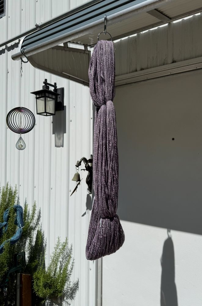 A grey and purple skein of handspun yarn hanging in the sunshine.