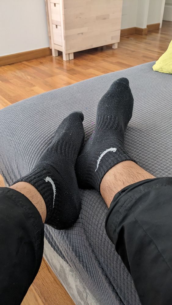 Dos pies sobre un sofá gris embutidos en calcetines negros y cortos