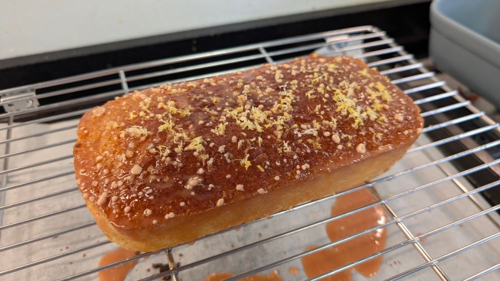 An orange and lemon loaf cake topped with citrus icing and more lemon zest, sitting on a cooling rack