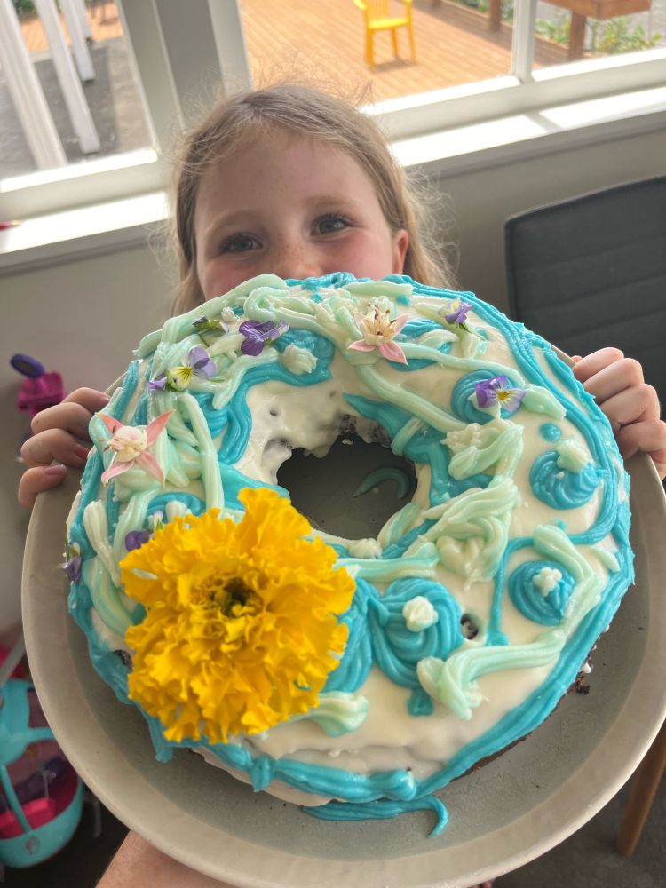 Small child holding up ring cake with white and pale blues icing and flowers on top