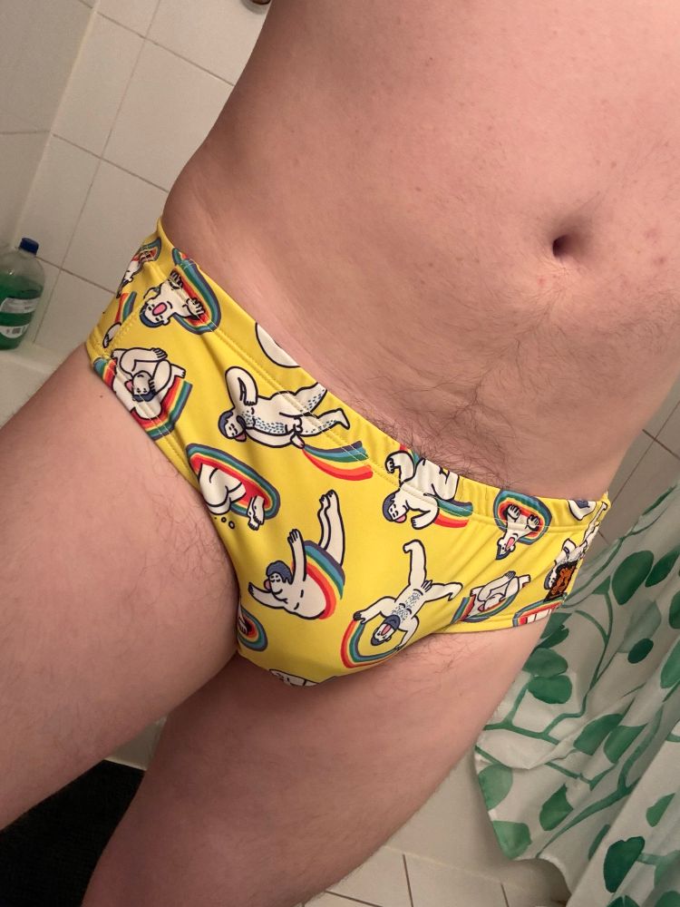 Man in a speedo that is yellow with images of a nude cartoon man in various poses with rainbows