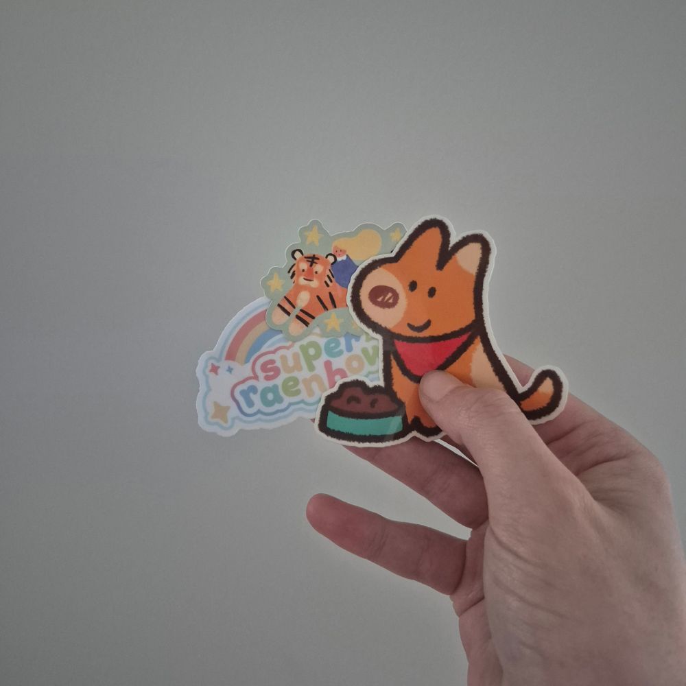 A hand holding three stickers by superaenbow.  A puppydog wearing a bandana with some chow, the shop owner logo with a pastel rainbow and a girl riding a tiger.